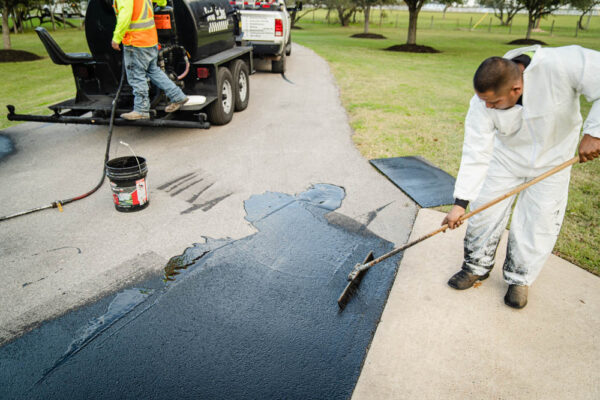 A paving worker is sealing asphalt cracks to prevent ice and water from entering and disturbing the integrity of the driveway.