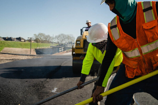 Paving workers using their shovels while adjusting new layer of asphalt in the construction of road.