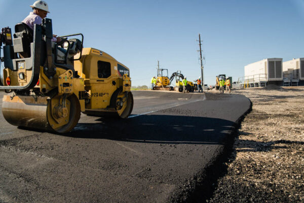 A man pressing down an asphalt road with a smaller road roller.