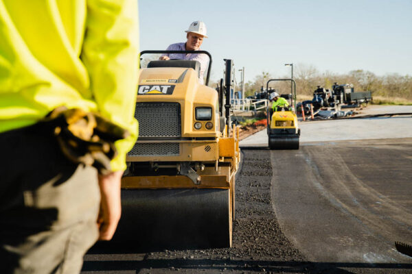 The worker leads the road roller to compact the asphalt laid out for the construction of a road.