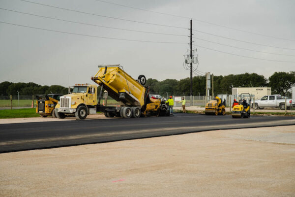 As asphalt is poured into an asphalt paver, road roller machines are ready to smooth out a new road.