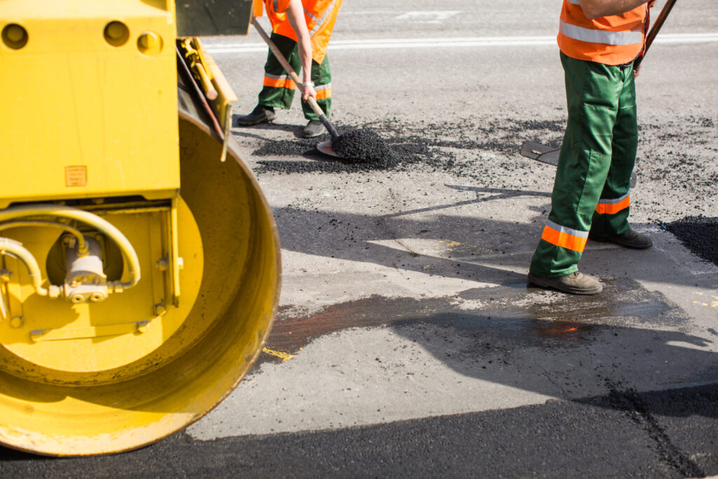 Workers on Asphalting paver machine during Road street repairing works. Street resurfacing. Fresh asphalt construction. Bad road
