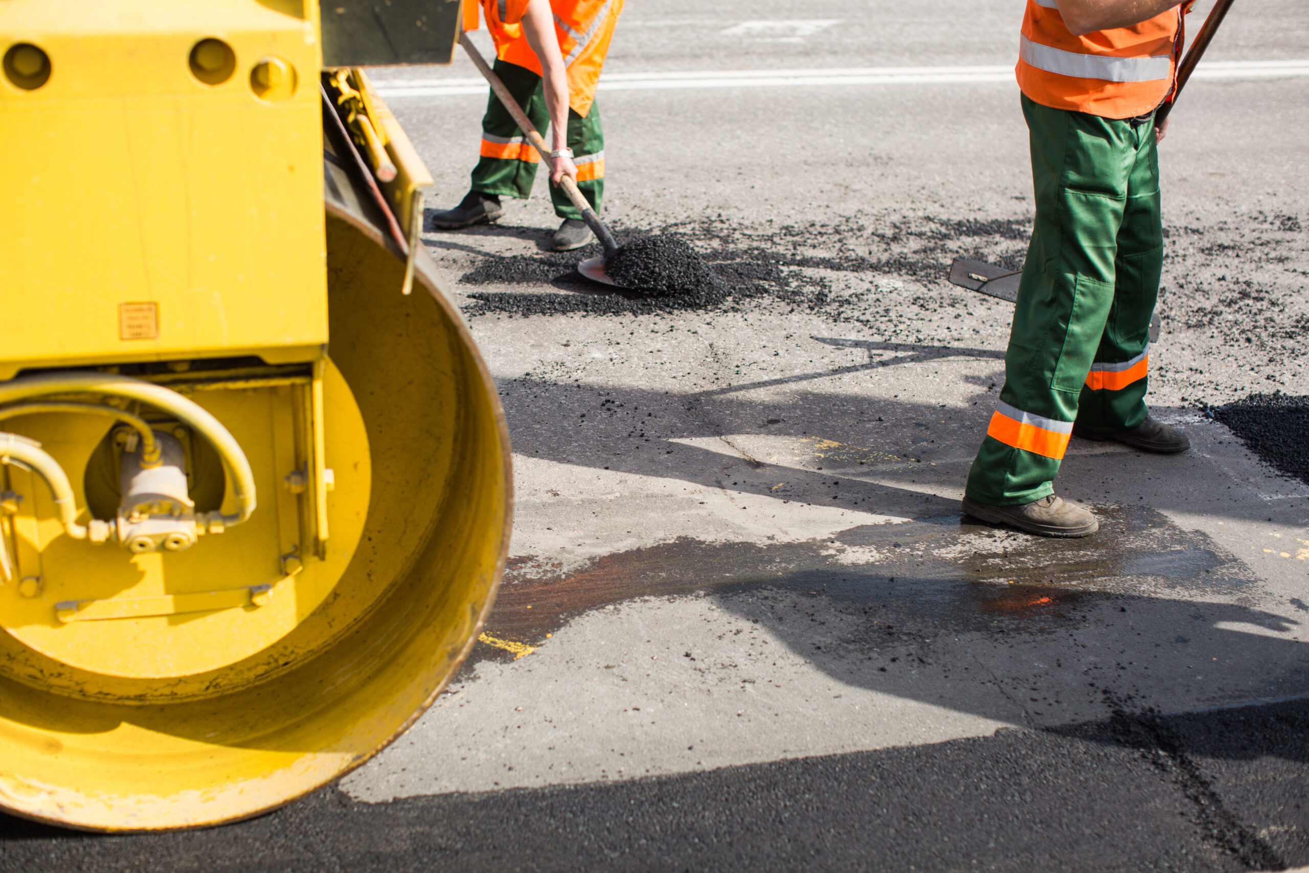 Workers on Asphalting paver machine during Road street repairing works. Street resurfacing. Fresh asphalt construction. Bad road